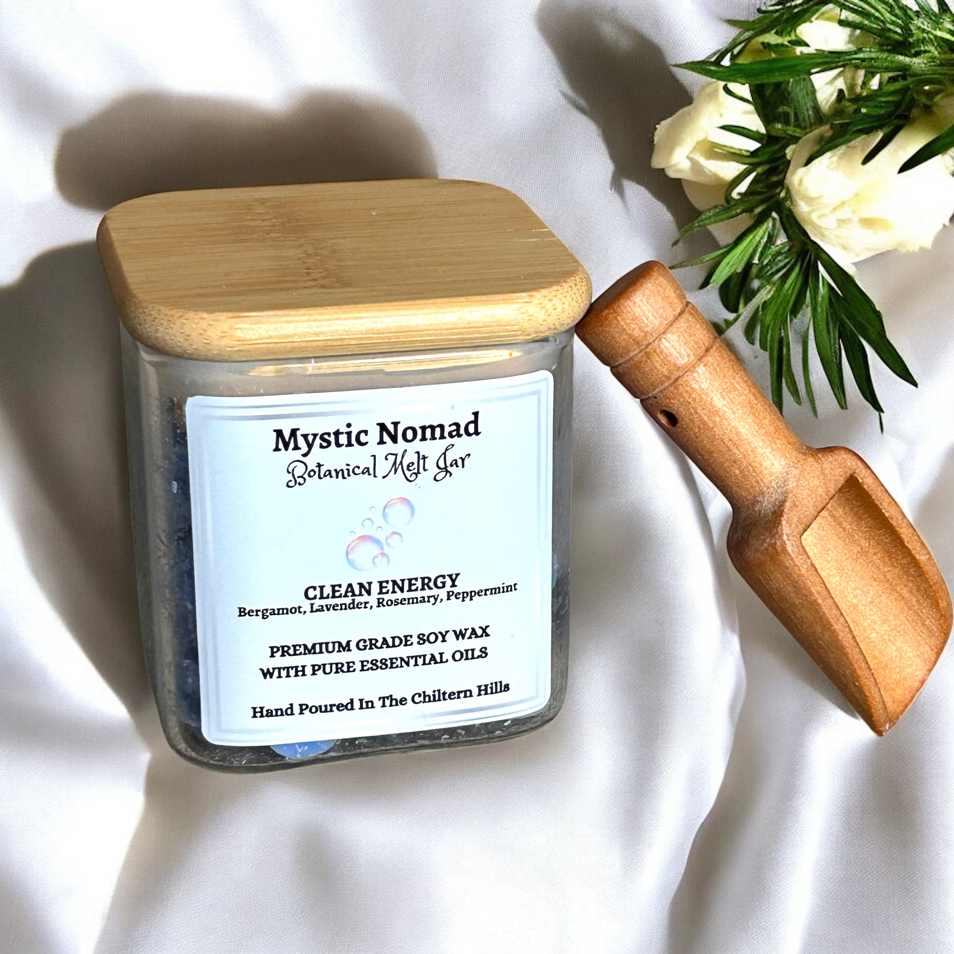 Lifestyle scene featuring Mystic Nomad Clean Energy aromatherapy wax melts in glass jar with bamboo lid, set on a wooden surface with fresh herbs and sunlight, creating a fresh, calming home environment
