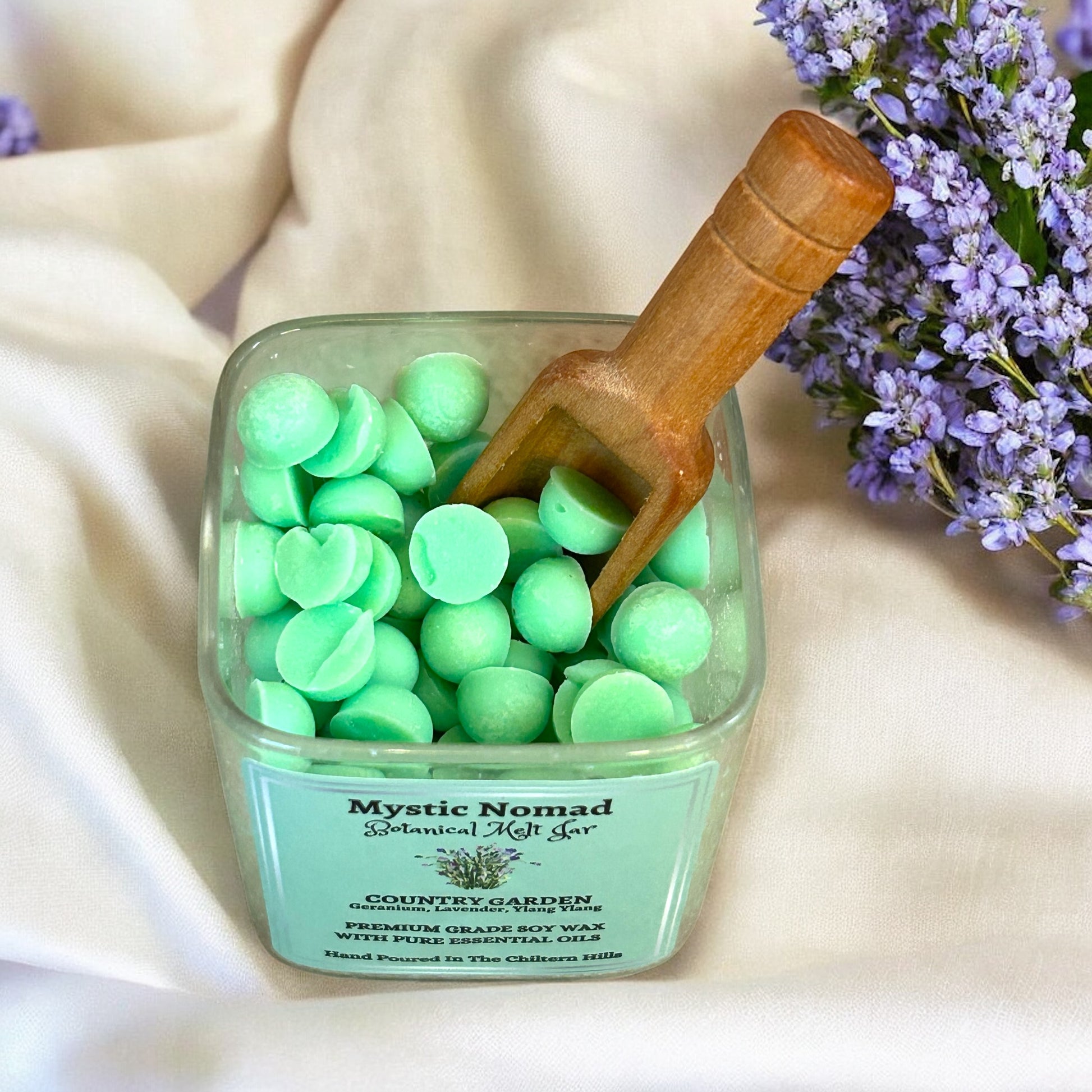 Open jar of Mystic Nomad Country Garden wax melts with wooden spoon, showing floral aromatherapy wax beads