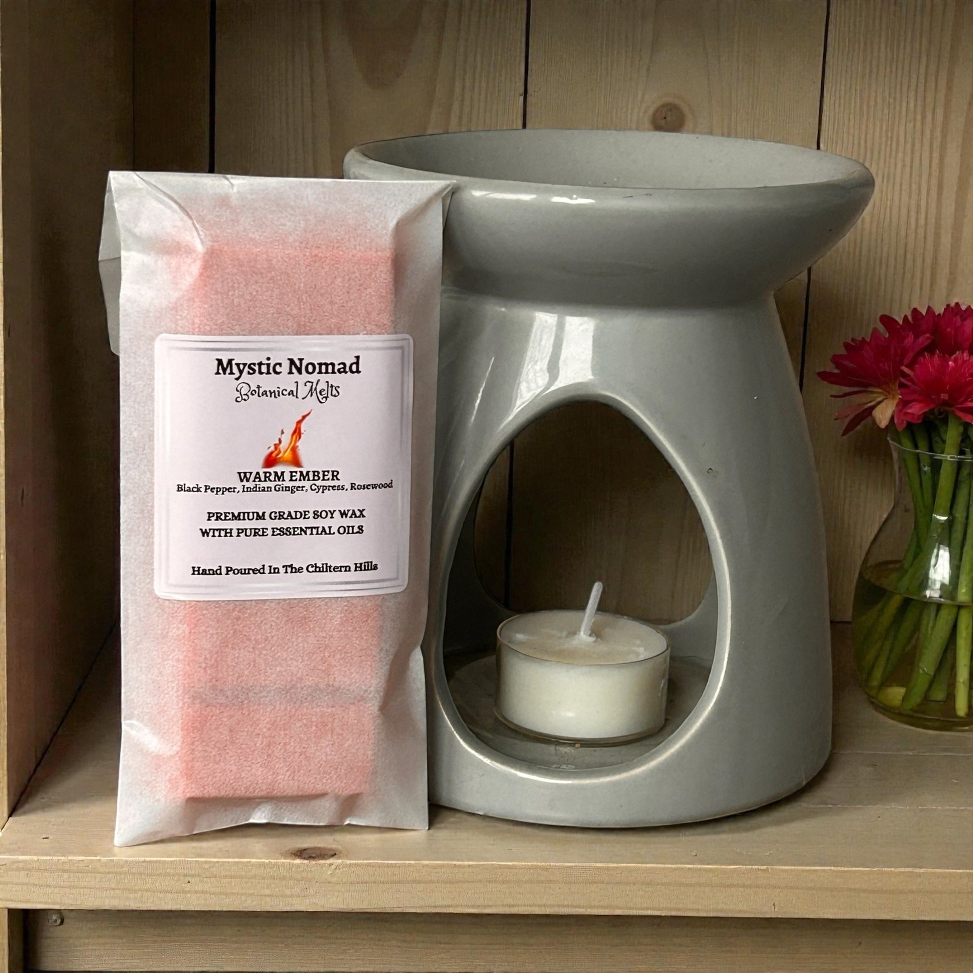 Warm Ember wax melt snap bar placed with  a ceramic wax melt burner on a shelf with flower showing aromatherapy vibe releasing a fireside-inspired, grounding aroma for mindfulness and meditation.